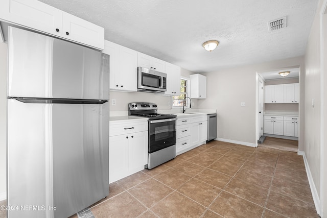 kitchen with sink, a textured ceiling, white cabinetry, stainless steel appliances, and tile patterned floors