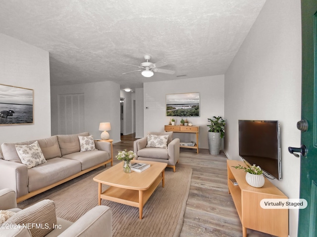 living room with a textured ceiling, light wood-type flooring, and ceiling fan