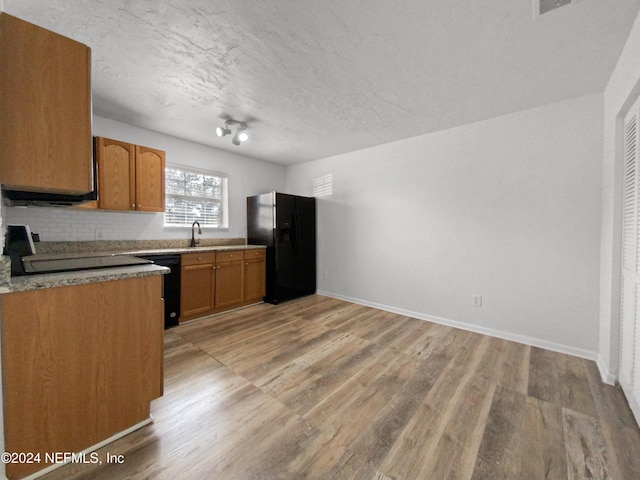 kitchen featuring black appliances, light wood finished floors, tasteful backsplash, a sink, and a textured ceiling