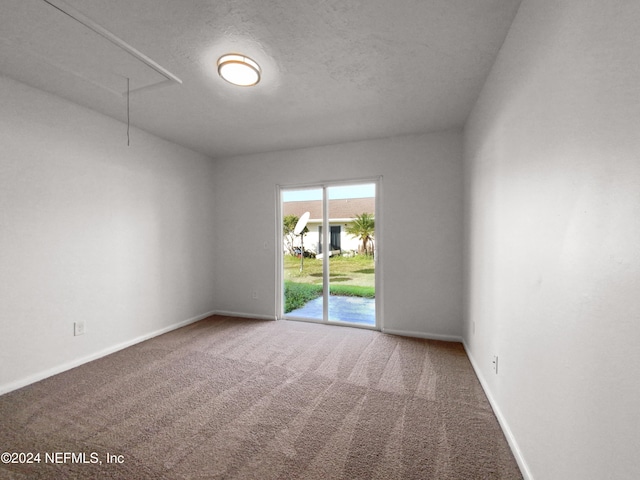 carpeted spare room featuring attic access and baseboards