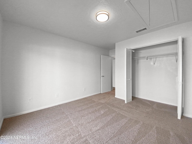 unfurnished bedroom with attic access, carpet floors, a closet, and baseboards