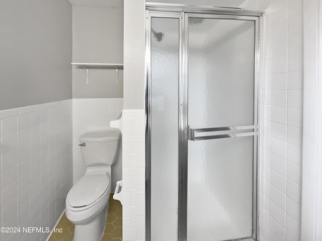 bathroom featuring toilet, tile walls, and a shower with door