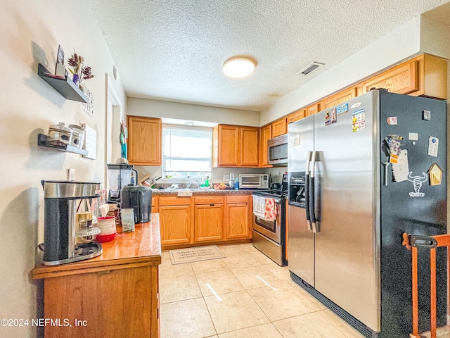 kitchen with a textured ceiling, light tile patterned flooring, and stainless steel appliances