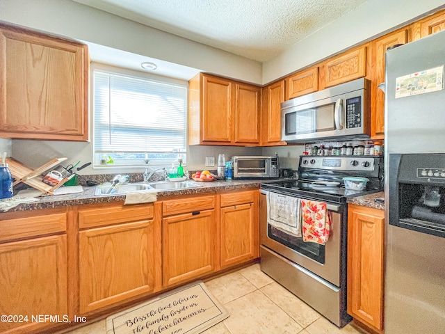 kitchen with appliances with stainless steel finishes, sink, light tile patterned flooring, and a textured ceiling