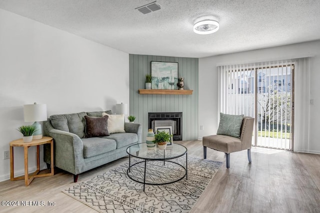 living room with a fireplace, a wealth of natural light, a textured ceiling, and light hardwood / wood-style flooring