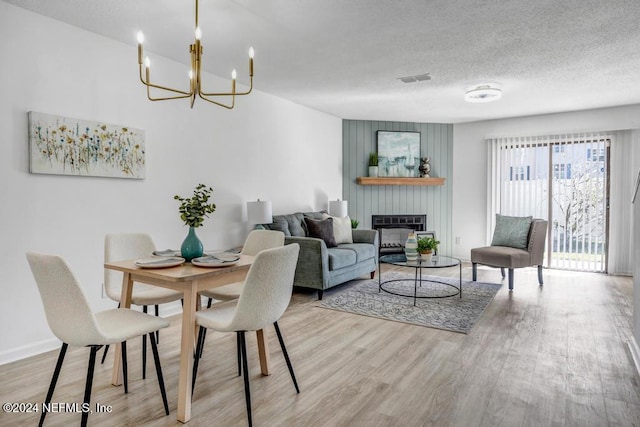 dining space with a fireplace, light hardwood / wood-style flooring, a textured ceiling, and a chandelier