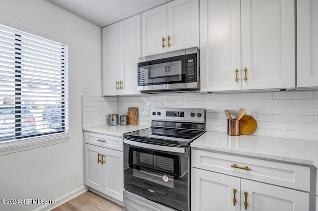 kitchen featuring tasteful backsplash, stainless steel appliances, light wood-type flooring, light stone countertops, and white cabinets