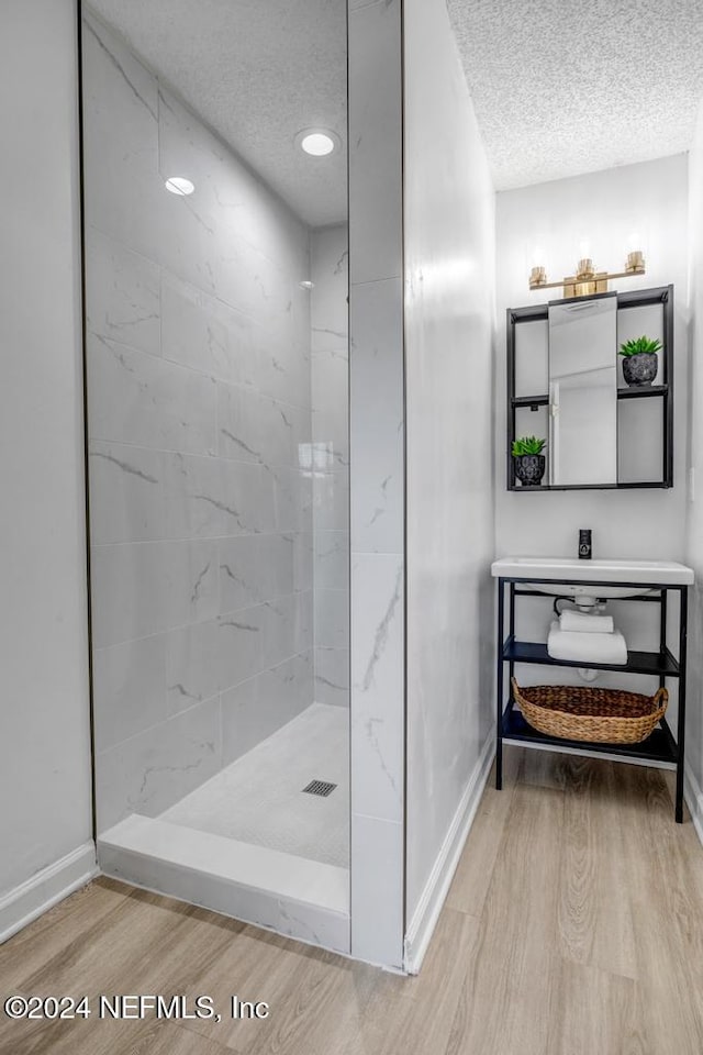 bathroom with wood-type flooring, tiled shower, and a textured ceiling