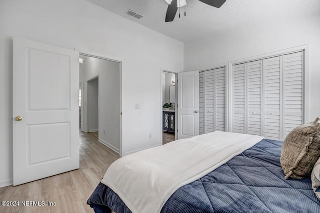 bedroom with a textured ceiling, light wood-type flooring, multiple closets, and ceiling fan