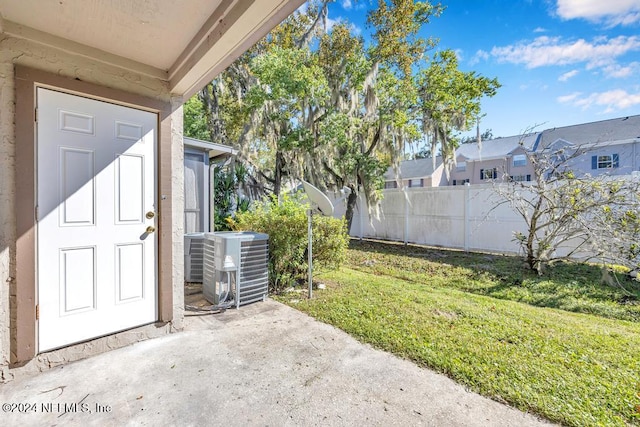 entrance to property with central AC unit, a lawn, and a patio area