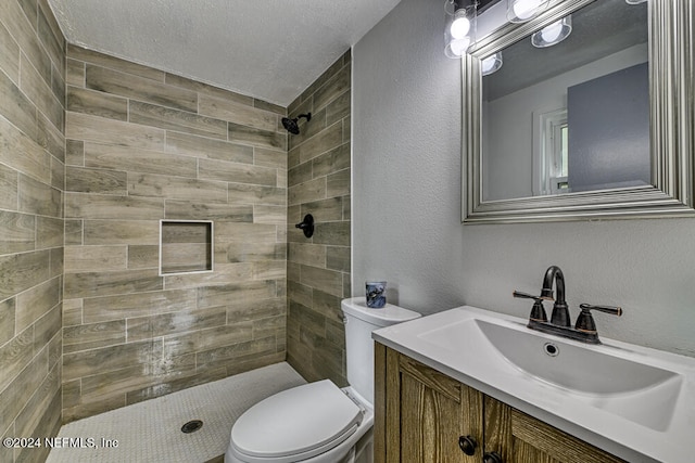 bathroom featuring vanity, toilet, a textured ceiling, and tiled shower