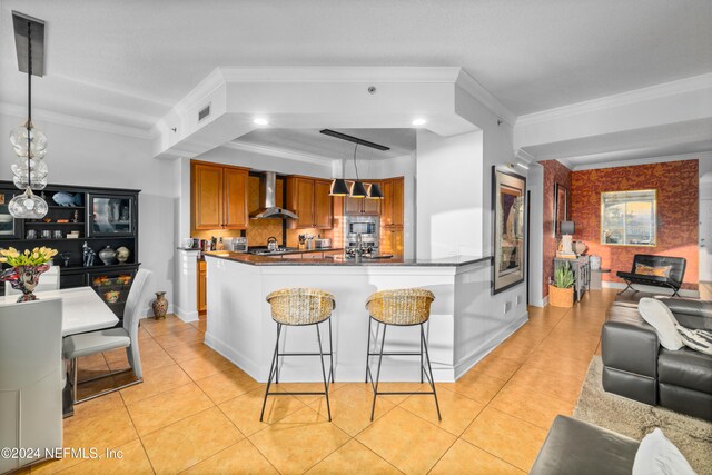 kitchen featuring wall chimney exhaust hood, a kitchen breakfast bar, hanging light fixtures, and light tile patterned floors