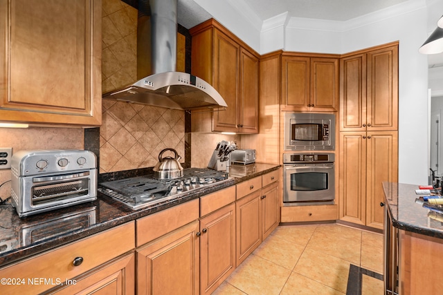 kitchen featuring wall chimney range hood, light tile patterned floors, dark stone counters, crown molding, and stainless steel appliances