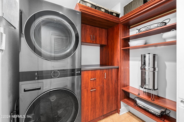 laundry area with cabinets, light tile patterned flooring, and stacked washer and clothes dryer