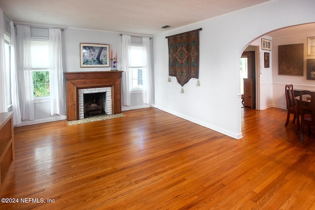 unfurnished living room featuring wood-type flooring, ornamental molding, and a brick fireplace