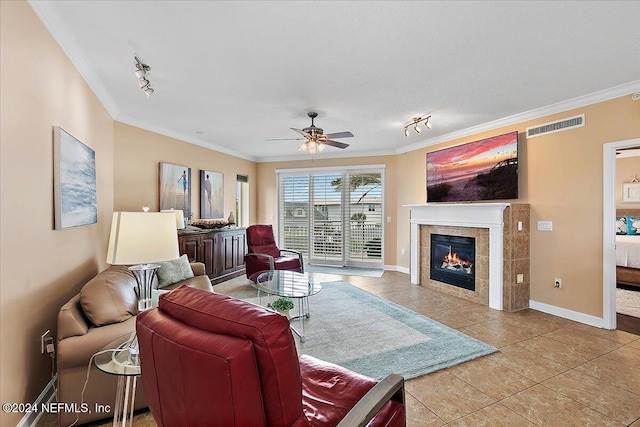 living room with light tile patterned floors, a tiled fireplace, ceiling fan, crown molding, and track lighting