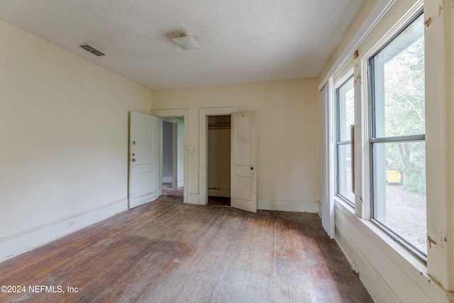 empty room with a healthy amount of sunlight, a textured ceiling, and dark hardwood / wood-style flooring