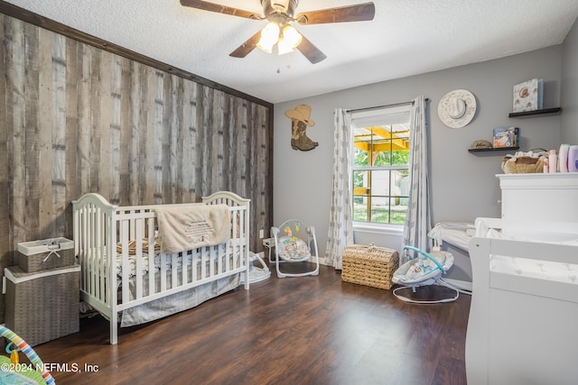 bedroom featuring a textured ceiling, a nursery area, dark hardwood / wood-style floors, and ceiling fan