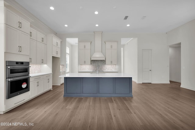 kitchen with white cabinetry, custom range hood, a center island with sink, and light wood-type flooring