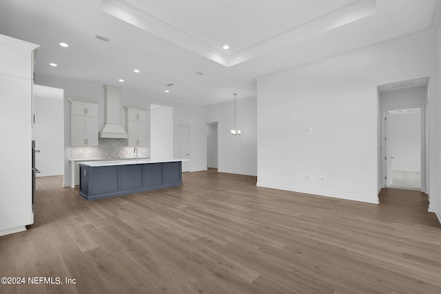 unfurnished living room with sink, crown molding, a tray ceiling, and light hardwood / wood-style flooring