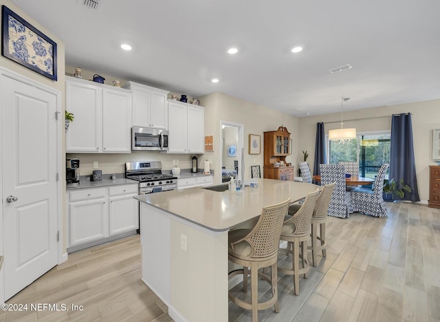 kitchen with decorative light fixtures, white cabinets, a kitchen island with sink, and appliances with stainless steel finishes