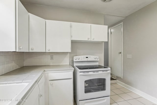 kitchen featuring light tile patterned floors, decorative backsplash, tile counters, white cabinets, and electric range