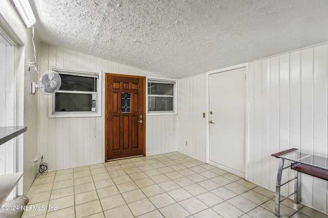 tiled entryway featuring wood walls, a textured ceiling, and vaulted ceiling