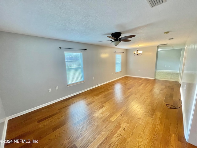 empty room with a textured ceiling, ceiling fan with notable chandelier, and light wood-type flooring