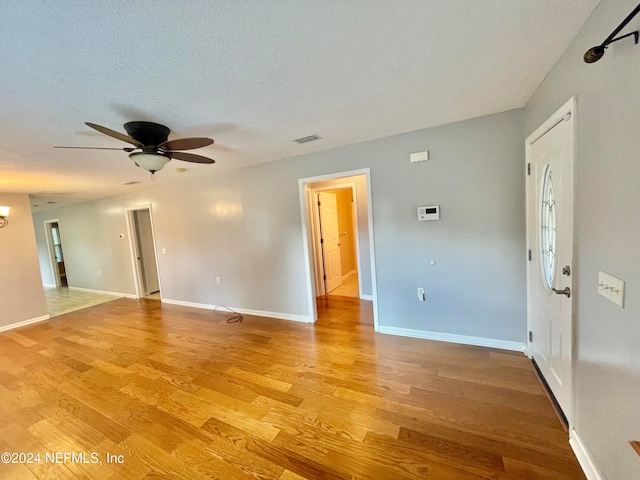 empty room with a textured ceiling, light wood-type flooring, and ceiling fan