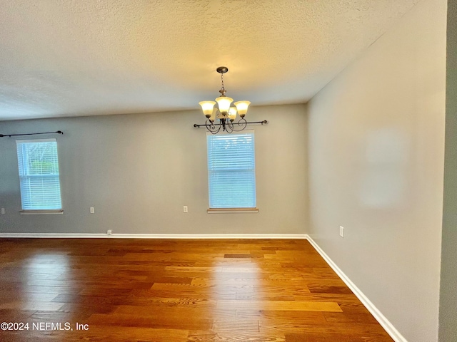 unfurnished room with a notable chandelier, a textured ceiling, and wood-type flooring