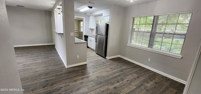 kitchen with light stone countertops, stainless steel fridge, white cabinets, and dark wood-type flooring