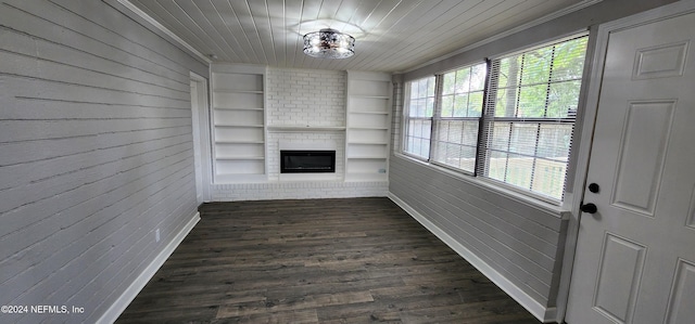 unfurnished living room featuring dark wood-type flooring, a fireplace, built in shelves, crown molding, and brick wall