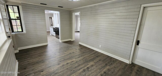 spare room featuring wood walls, dark hardwood / wood-style floors, and crown molding