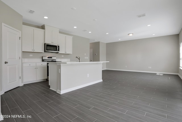 kitchen with a center island with sink, white cabinets, stove, and dark wood-type flooring