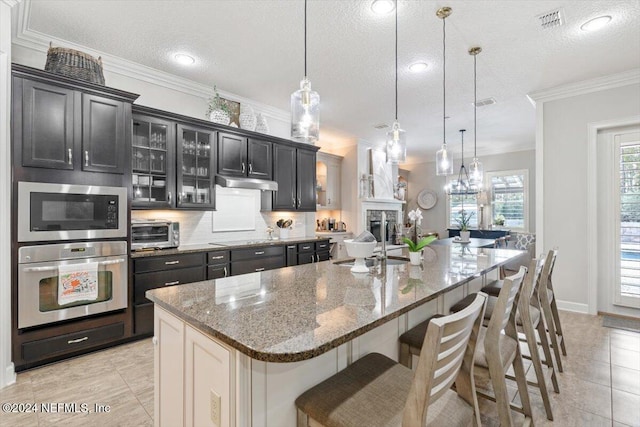 kitchen featuring a textured ceiling, stainless steel appliances, decorative light fixtures, and a large island with sink