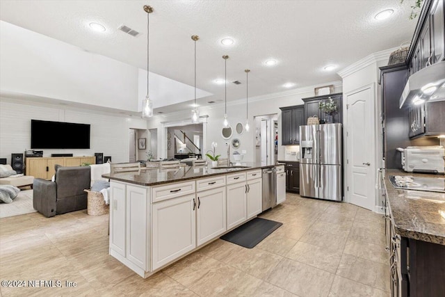 kitchen featuring stainless steel appliances, a center island with sink, ornamental molding, pendant lighting, and a textured ceiling