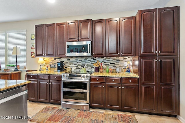 kitchen featuring light stone countertops, appliances with stainless steel finishes, light tile patterned floors, and decorative backsplash