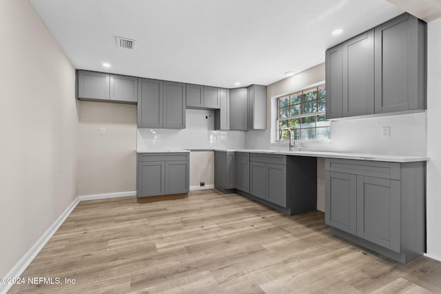 kitchen with gray cabinetry, decorative backsplash, and light wood-type flooring