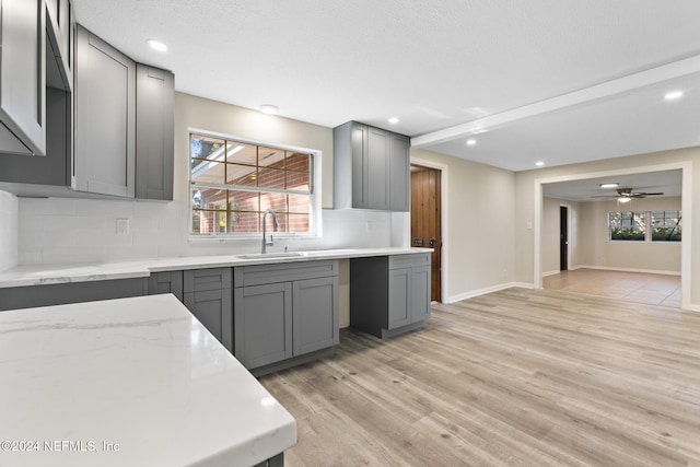 kitchen with decorative backsplash, light hardwood / wood-style flooring, sink, gray cabinets, and ceiling fan