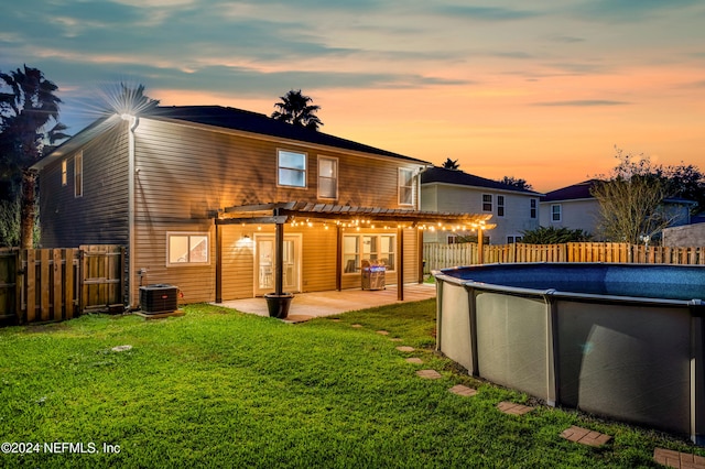 back house at dusk featuring a fenced in pool, a pergola, cooling unit, a patio, and a lawn