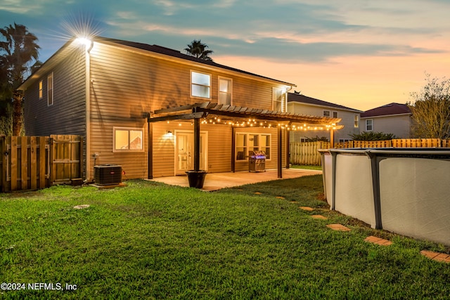 back house at dusk featuring cooling unit, a pergola, a patio, and a yard