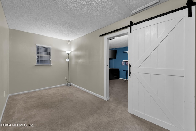 unfurnished room with a barn door, light colored carpet, and a textured ceiling