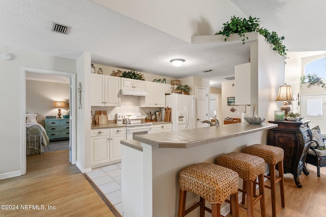 kitchen with white appliances, light wood-type flooring, a textured ceiling, white cabinetry, and a breakfast bar area