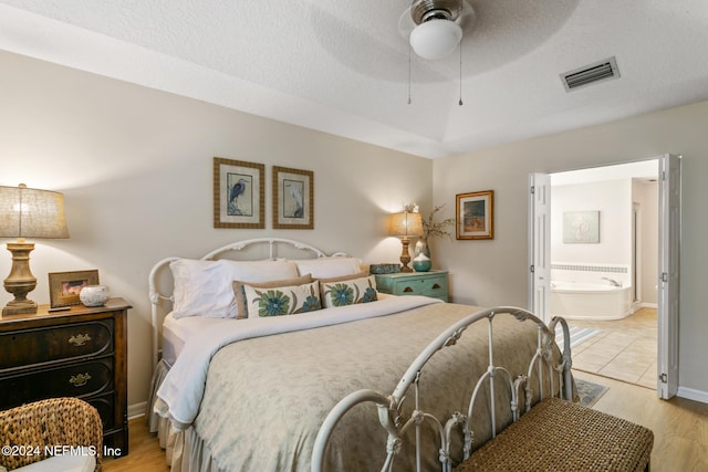 bedroom featuring ensuite bath, a textured ceiling, light hardwood / wood-style floors, and ceiling fan