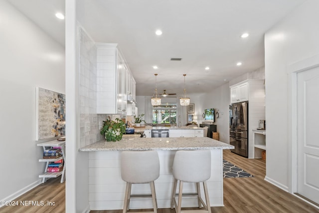 kitchen featuring light hardwood / wood-style flooring, kitchen peninsula, stainless steel appliances, pendant lighting, and white cabinets