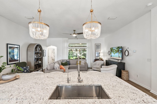 kitchen with decorative light fixtures, light stone counters, ceiling fan with notable chandelier, and dark hardwood / wood-style flooring