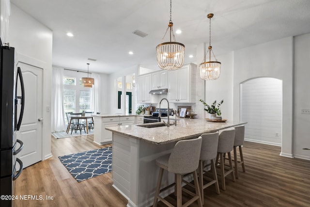 kitchen with white cabinets, decorative light fixtures, black fridge, and a kitchen island with sink