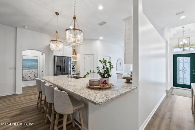 kitchen featuring stainless steel fridge, white cabinets, hanging light fixtures, light stone counters, and sink