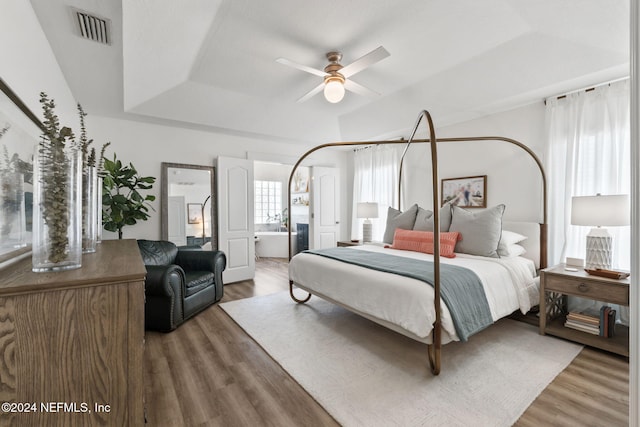 bedroom with hardwood / wood-style floors, ceiling fan, connected bathroom, and a raised ceiling