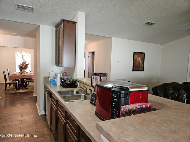 kitchen featuring sink, a textured ceiling, stainless steel dishwasher, an inviting chandelier, and dark hardwood / wood-style floors